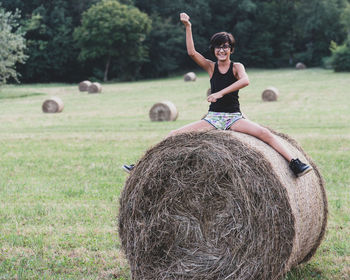 Full length portrait of smiling girl sitting on hay bale at farm