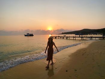 Rear view of woman on beach against sky during sunset