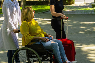 Woman holding suitcase while doctor pushing patient on wheelchair