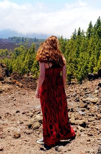 Rear view of teenage girl standing on field against sky