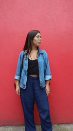 Young woman looking away while standing against wall