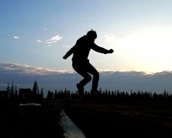 Silhouette man jumping on road against sky at night