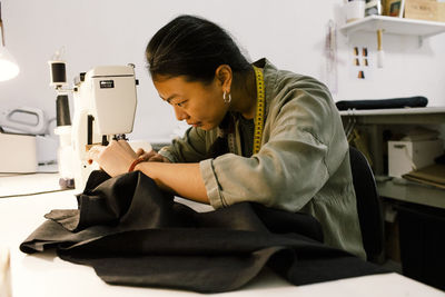 Focused seamstress stitching clothes using sewing machine while working at store