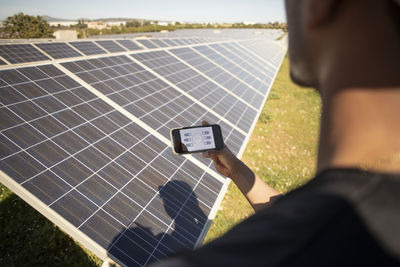 Male engineer programming solar panels through smart phone app at power station