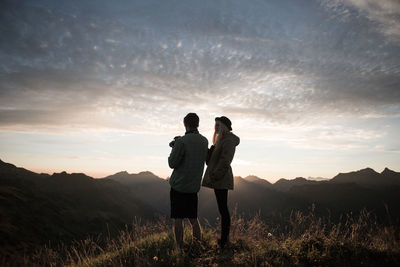 Couple standing on field against sky during sunset