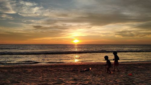 Silhouette people on beach against sky during sunset