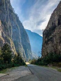 Road amidst trees and mountains against sky