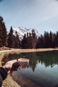 Man holding ice cream by lake against sky