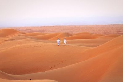 People on sand dune in desert against sky