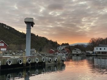Buildings by river against sky during sunset