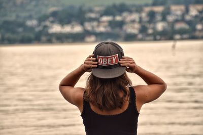 Rear view of woman holding hat while standing on beach