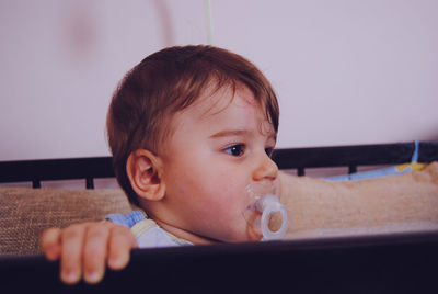 Close-up of baby boy with pacifier in mouth looking away at home