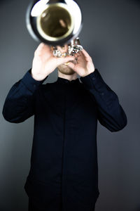 Midsection of man holding hat while standing against gray background