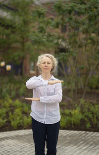 Portrait of woman gesturing while standing on footpath against buildings