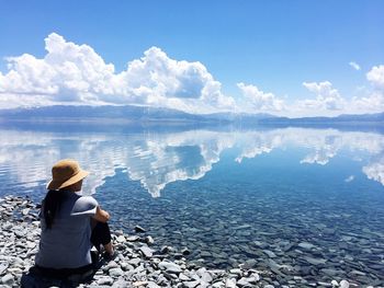 Rear view of woman sitting on lakeshore