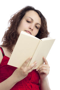 Portrait of young woman reading book against white background