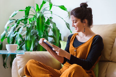 Smiling woman reading book while sitting on sofa at home