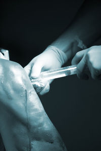 Cropped hands of doctor injecting syringe on patient knee in operating room