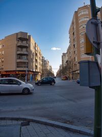 Cars on city street by buildings against sky