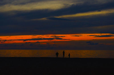 Silhouette people on beach against sky during sunset