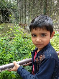 Portrait of boy on fence against plants