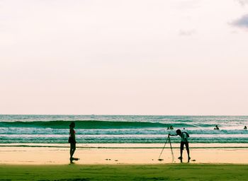 People standing on beach against clear sky