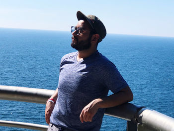 Young man looking away while standing by sea against sky