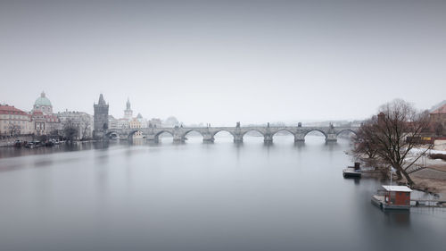 Charles bridge over vltava river against sky in city during foggy weather