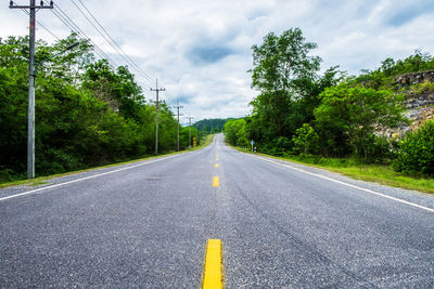 Empty road amidst trees against sky