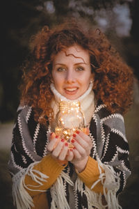 Portrait of young woman holding illuminated string lights in jar