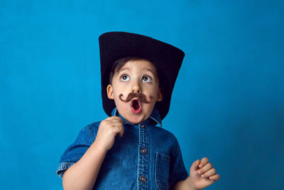 Funny cowboy boy with a mustache and a hat stands in the studio on a blue background