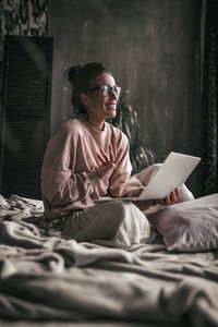 Young woman using mobile phone while sitting on bed