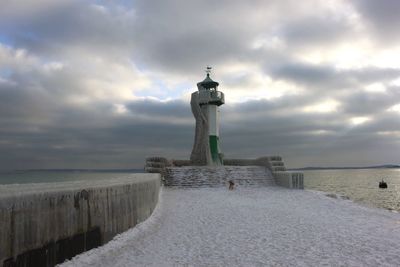 Lighthouse by sea against cloudy sky