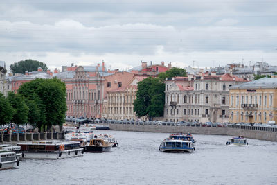 Sailboats in river by buildings in city against sky