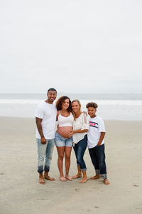 Family posing for maternity photos on beach