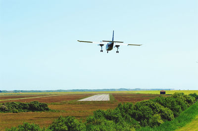 Airplane flying over field against clear sky