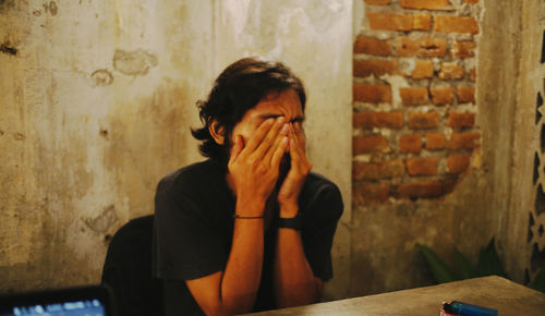 Portrait of young man sitting against wall