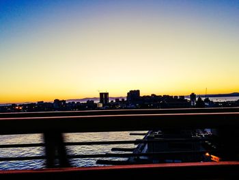 Silhouette buildings by river against sky during sunset