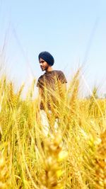 Young man standing on wheat field against clear sky