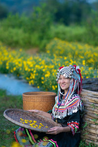 Portrait of woman in traditional clothing holding straw basket sitting at farm