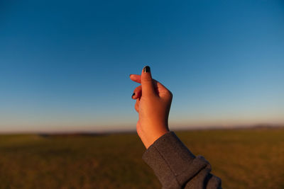 Close-up of hand on field against blue sky