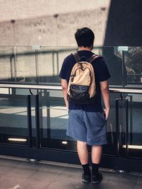 Rear view of young man standing against railings and wall