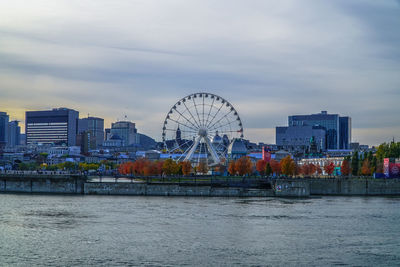 Ferris wheel by river in city against sky