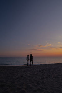 Men on beach against sky during sunset