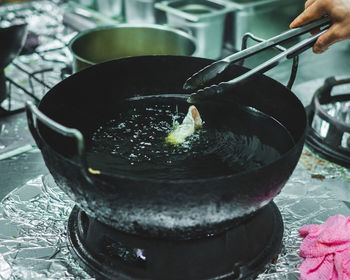 Cropped hand of woman frying food in cooking oil on stove