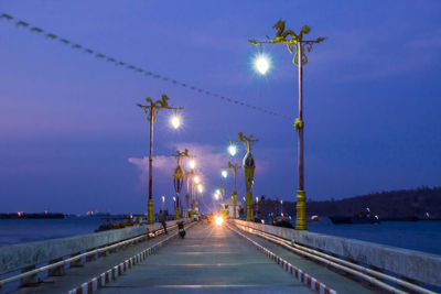 Illuminated street lights by road against sky at night