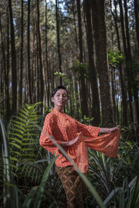 Portrait of woman standing by tree trunk in forest