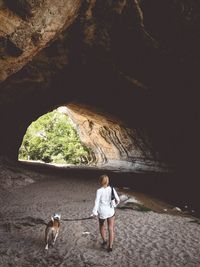 Rear view full length of woman with dog on sand entering cave