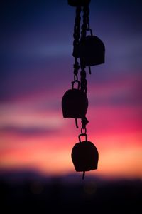 Close-up of silhouette padlocks hanging against sky at sunset