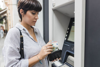 Young woman counting money from purse at atm machine